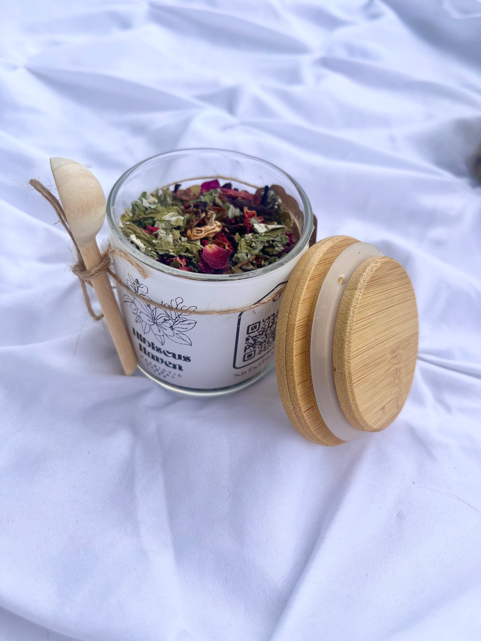 Glass jar with dried herbs and a wooden spoon on a white fabric background