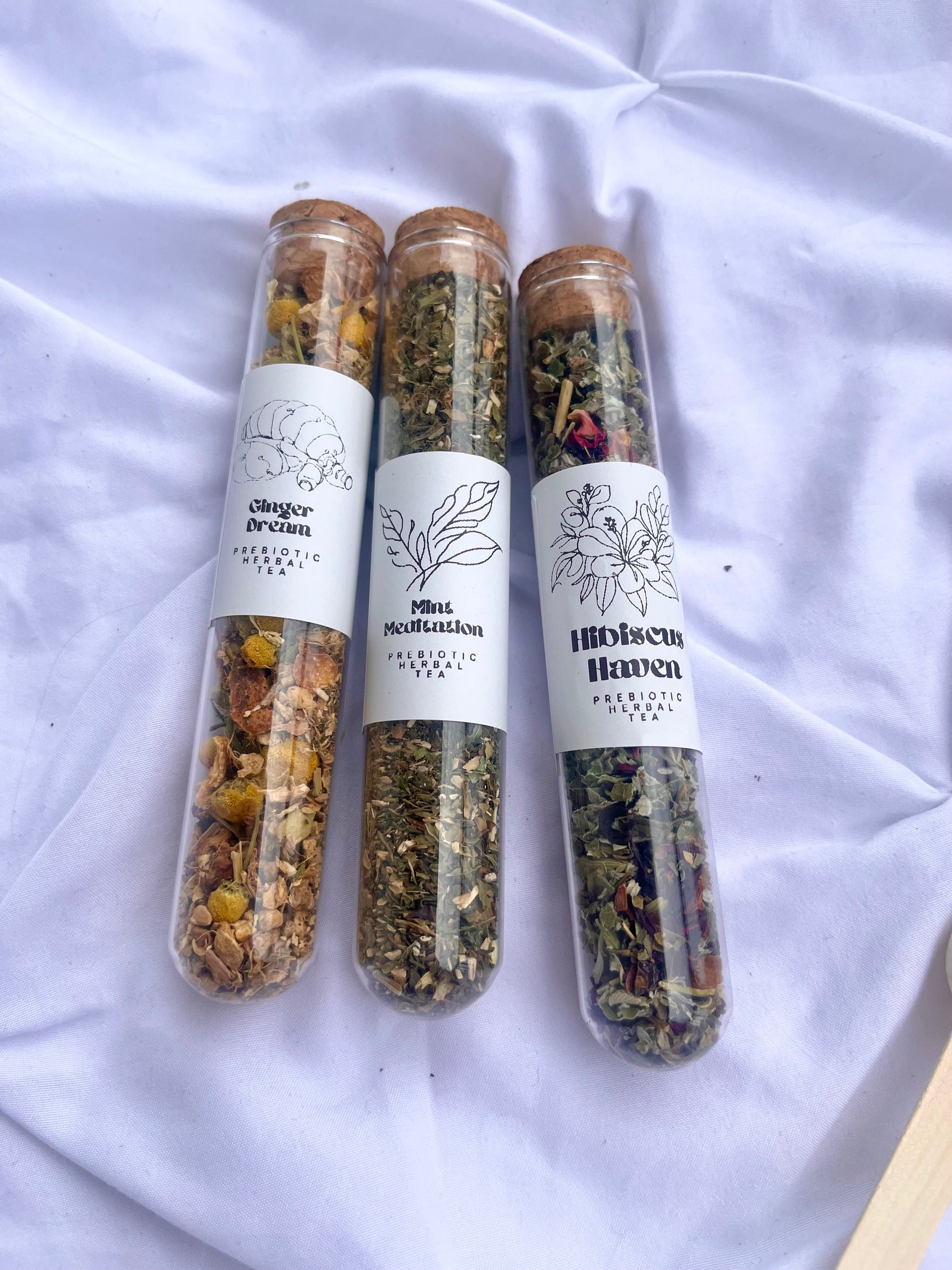 Three transparent tubes filled with herbs or spices, each labeled with different brands, on a white fabric background.