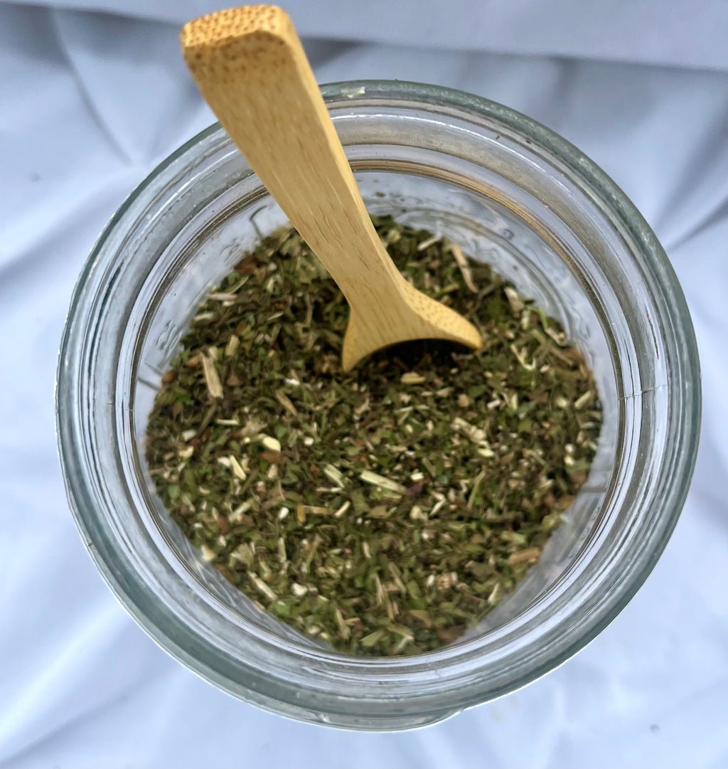 Glass jar filled with dried herbs and a wooden spoon on a white background