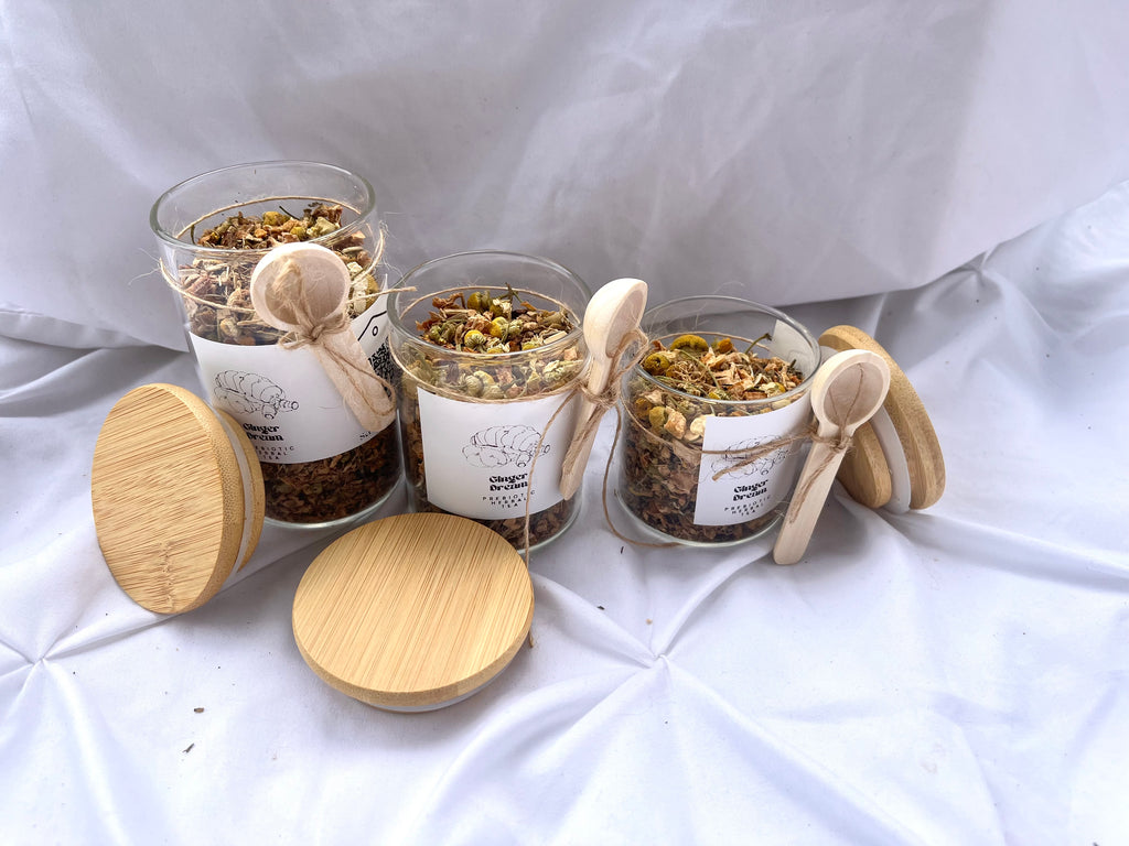 Three glass jars with wooden lids and spoons on a white fabric background