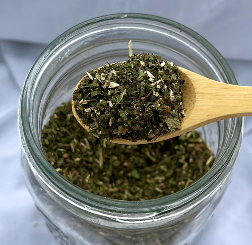 Dried herbs on a wooden spoon over a glass jar with a white background