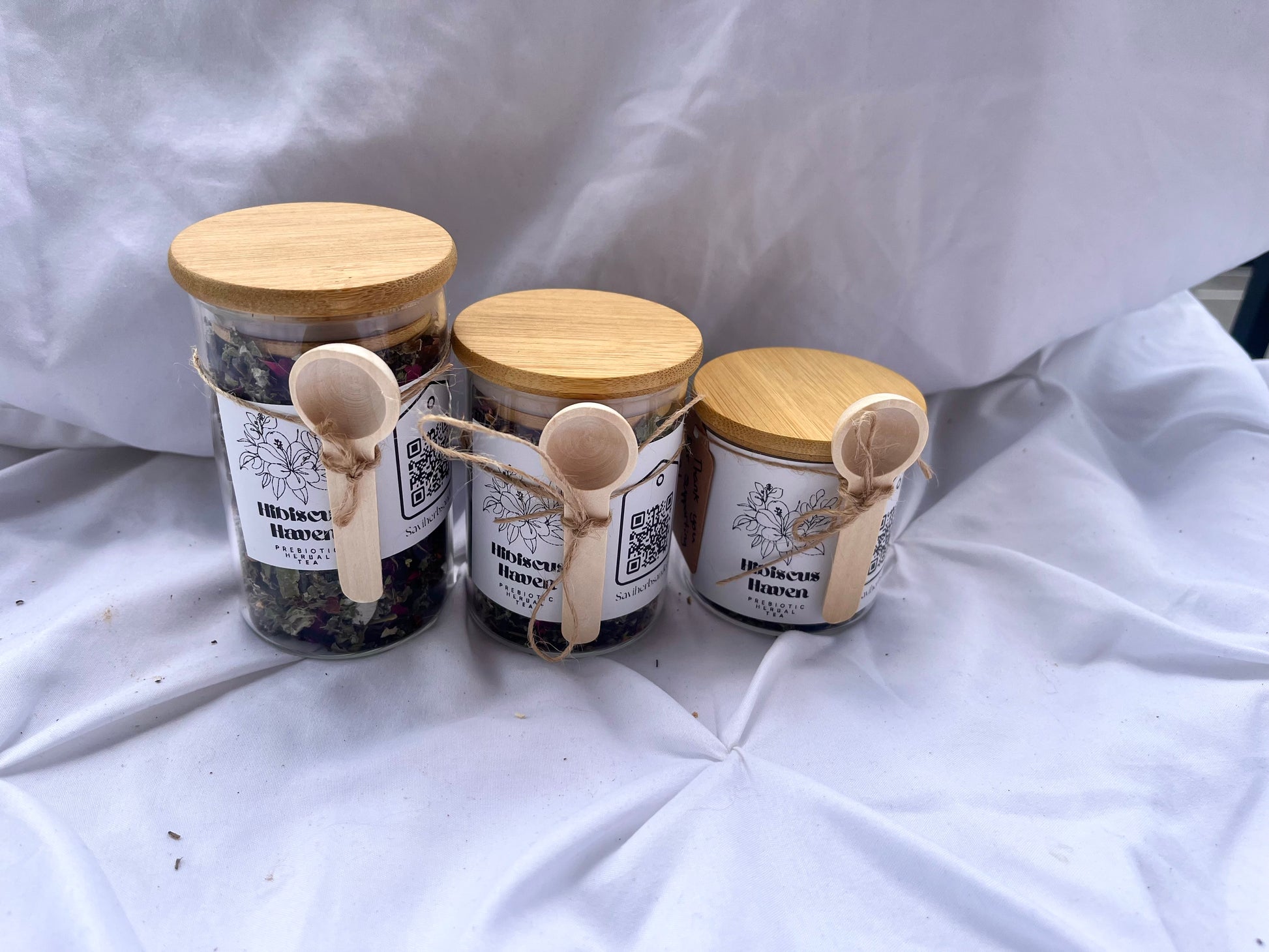 Three jars of honey with wooden lids on a white fabric background
