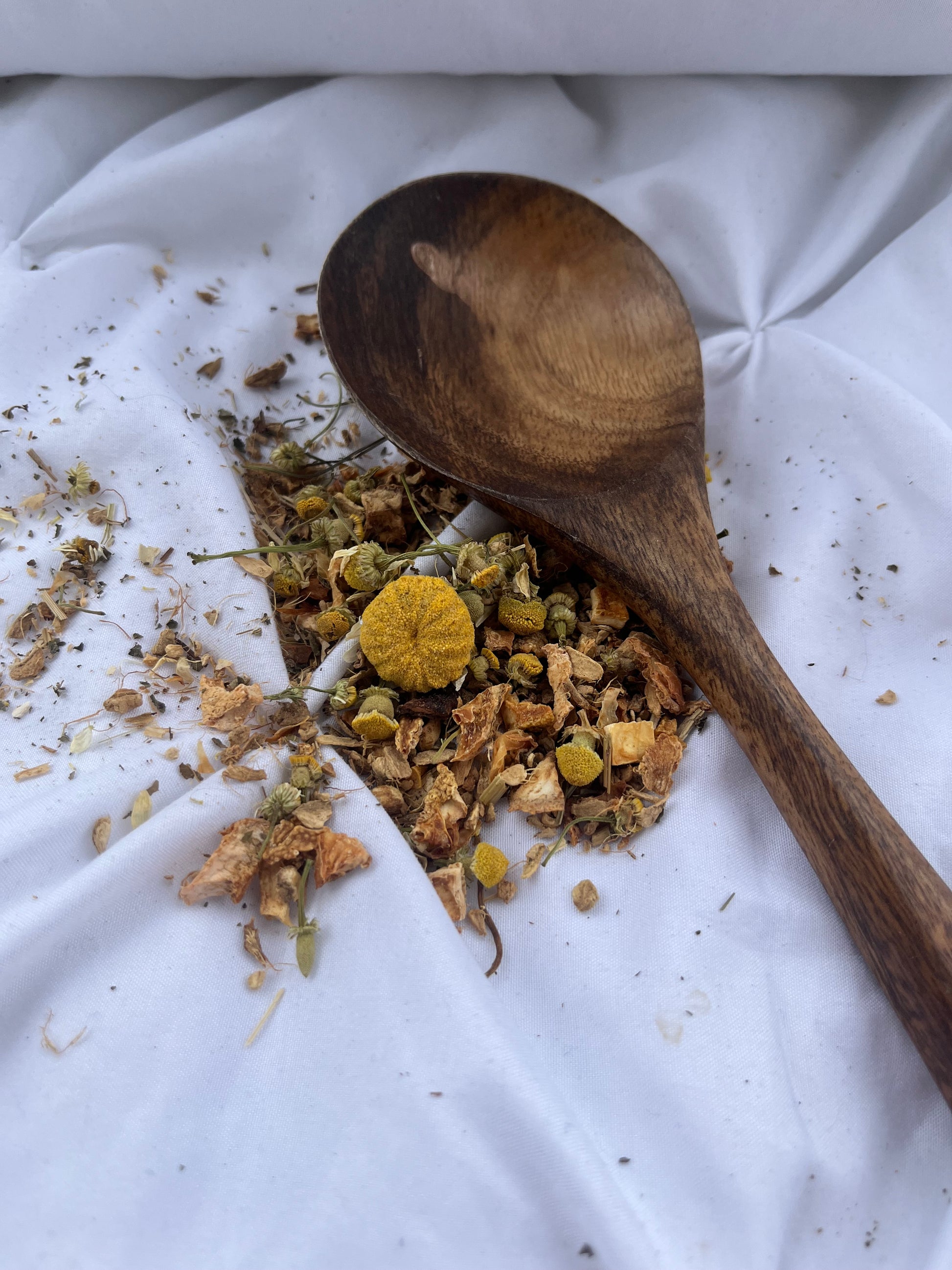 Wooden spoon with dried herbs on a white fabric background