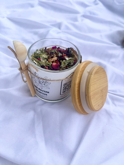 Glass jar with dried herbs and a wooden spoon on a white fabric background