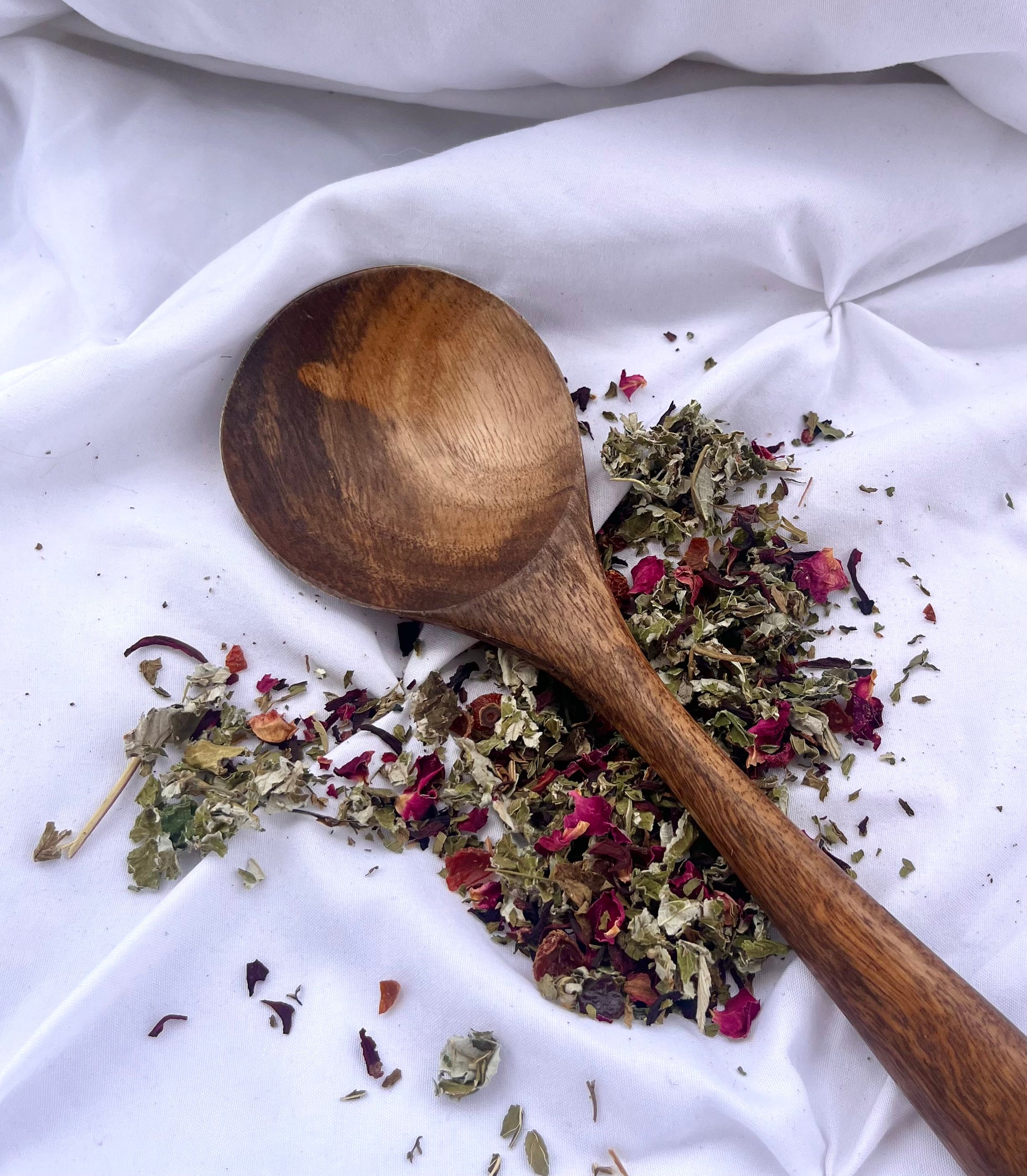 Wooden spoon with dried herbs on a white fabric background