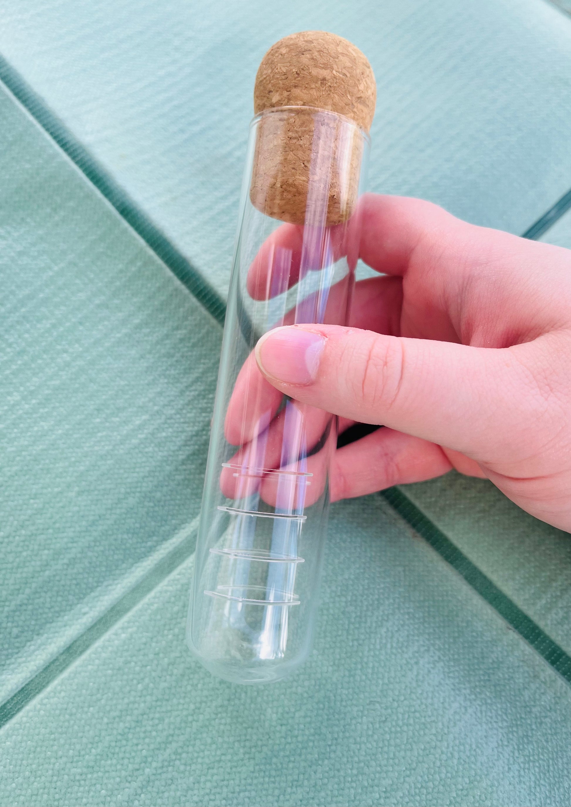 Clear glass bottle with cork stopper held by a hand on a light green surface